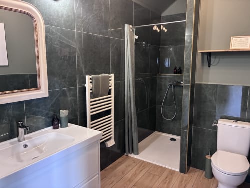 Salle de bain moderne du gîte Le Clos d'Émilie à Saint-Marcel : carrelage en marbre noir, lavabo blanc, douche pluie et chauffage