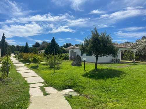 Viale del giardino di Resort Baia Cea con bungalow bianchi, rigogliosa vegetazione e salici piangenti a Bari Sardo