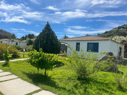 Resort Baia Cea a Bari Sardo: biancheria bungalow con porte blu circondato da rigogliosi giardini e paesaggio mediterraneo