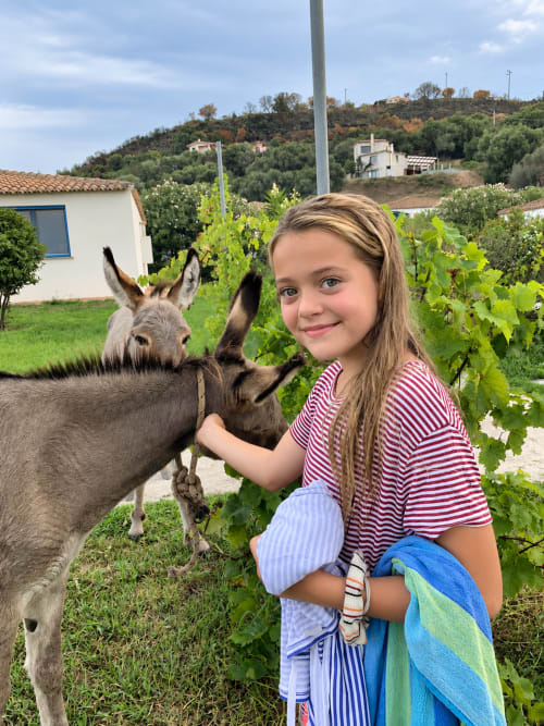 Ragazza che accarezza un asino al Resort Baia Cea a Bari Sardo, Sardegna con vigneti e case sulla collina