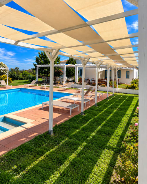 Area piscina del Resort Baia Cea con pergolato ombreggiante, lettini e edificio bianco a Bari Sardo