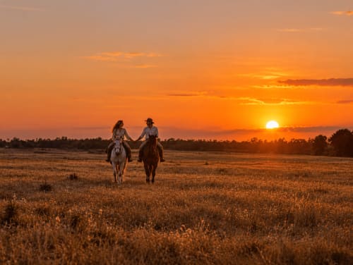 Dos jinetes de la mano al atardecer en la campiña de Guadalupe, Cáceres, cerca de El descanso del peregrino.