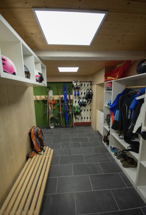 Salle de rangement de l'équipement aux Chalets d'Aline avec skis, chaussures et équipement d'hiver organisés sur les murs et étagères