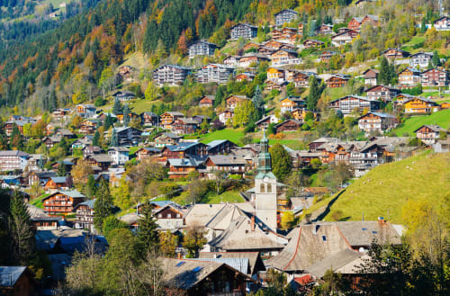 Vue aérienne du village de Morzine avec ses chalets traditionnels nichés dans un paysage alpin forestier, clocher d'église visible