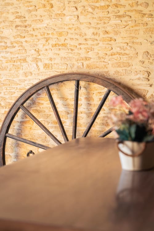 Roue de chariot rustique en bois contre un mur de briques crème au Domaine Du Grand Fort, chambre d'hôtes en Normandie