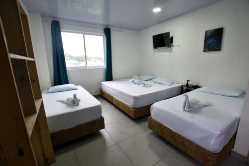 Habitación luminosa con tres camas, televisión y ventana con vista al mar en Vamos pa San Andrés Isla, Colombia