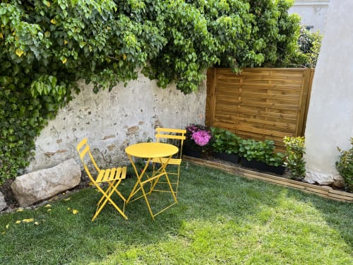 Cozy garden courtyard at Gites Les Glycines du Vexin with yellow bistro chairs, ivy-covered walls, and blooming flowers in