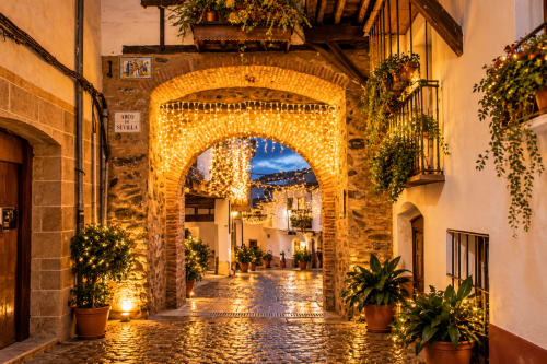 Arco de ladrillos iluminado en el centro histórico de Guadalupe, Cáceres al atardecer con macetas y calle empedrada