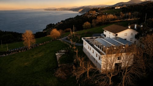 Moderno hotel rural con paneles solares con vistas a la costa vasca al atardecer, Mutriku, España. Ladera verde y vista al mar.