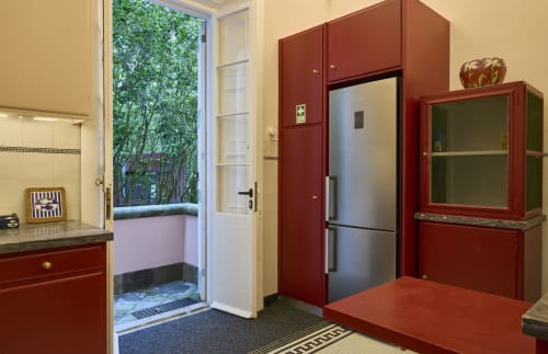 Cozinha rústica moderna com armários vermelhos, eletrodomésticos em aço inoxidável e porta com vista para o jardim na Casa da Lagoa, Furnas