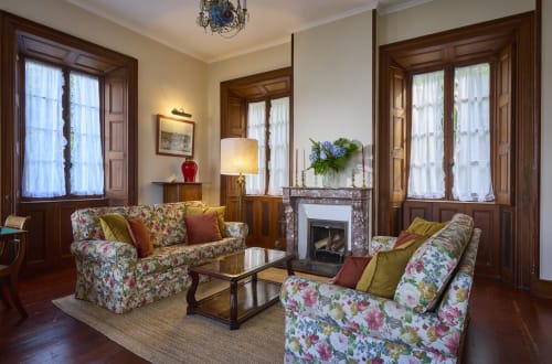 Elegante sala de estar da Casa da Lagoa em Furnas com sofás florais, lareira e portas de madeira com vista para o lago.
