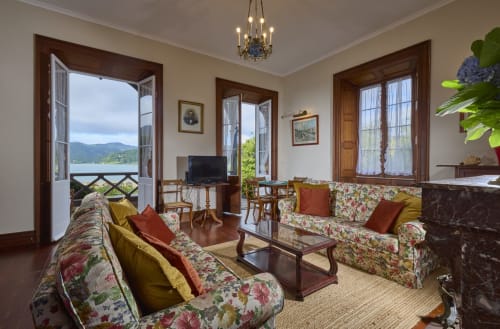 Elegante sala de estar da Quinta da Lagoa em Furnas, com sofás florais, vista do lago pelas portas abertas e decoração tradicional