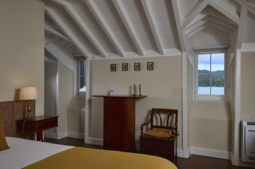 Quarto luminoso da casa de campo em São Miguel com vigas aparentes, móveis em madeira escura, roupa de cama amarela e vista para o lago
