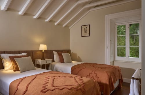 Quarto claro com camas de solteiro e roupa de cama em terracota na Casa da Lagoa, Furnas, com portas para vista do lago