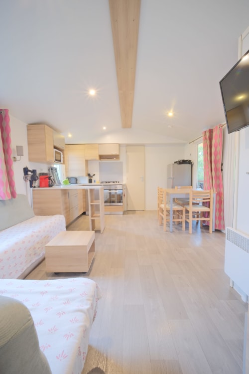 Intérieur lumineux et moderne du mobilhome à Annick Vias Plage avec cuisine en bois, salle à manger, lits, TV et rideaux roses