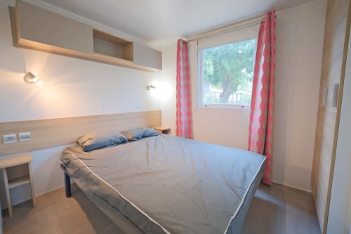 Chambre lumineuse du cottage Annick Mobilhome à Vias Plage avec lit queen-size, rideaux roses, vue mer et équipements modernes