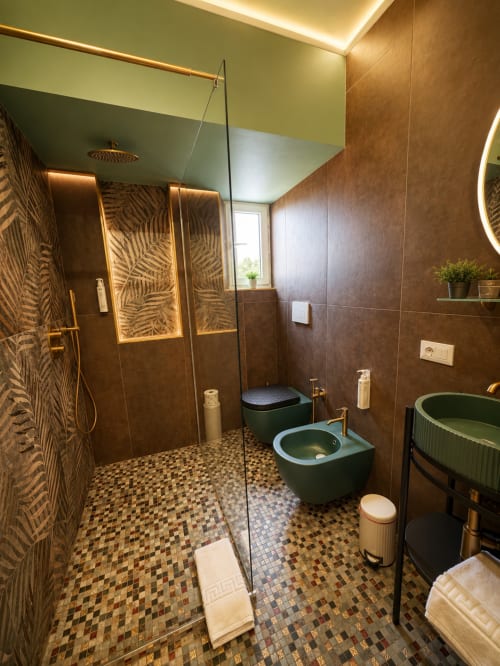 Lussuoso bagno dell'hotel Habemus con doccia walk-in, finiture verdi, specchio riscaldato, dettagli dorati e pavimento in mosaico