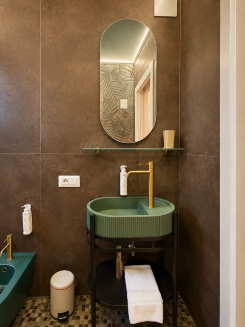 Bagno moderno dell'hotel Habemus a Rocca di Papa con lavabo verde, rubinetto in ottone, specchio ovale e piastrelle marroni
