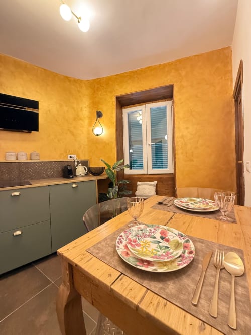 Luminosa zona cucina-pranzo dell'hotel Habemus a Rocca di Papa con tavolo in legno, piatti floreali e dettagli verde moderno