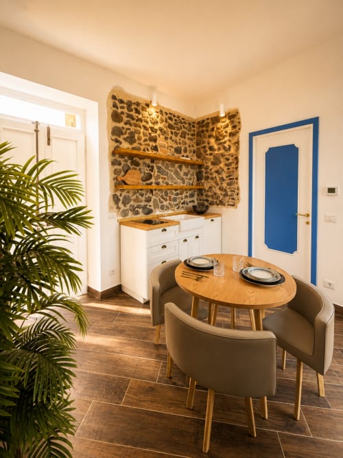 Zona pranzo moderna dell'appartamento Fronda presso l'hotel Habemus con tavolo in legno, sedie beige, muro in pietra e porta blu
