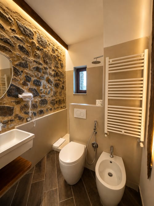 Bagno moderno dell'hotel Habemus a Rocca di Papa con parete in pietra, toilette, bidet, scaldasalviette e illuminazione