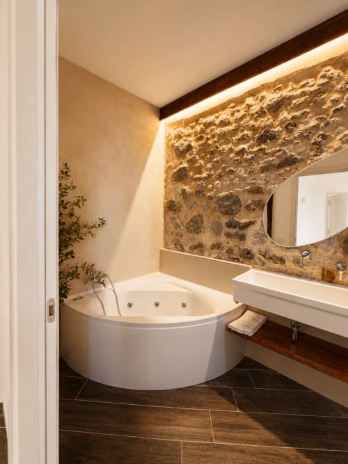 Lussuoso bagno con vasca idromassaggio angolare, parete in pietra, vanità in marmo e illuminazione ambientale nell'appartamento Fronda di Habemus