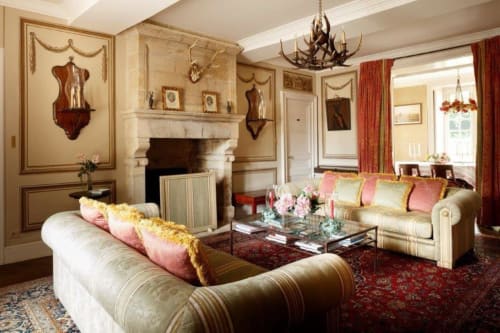 Élégant salon du Château de Servigny avec canapé crème, cheminée, lustre en bois de cerf et décor rouge