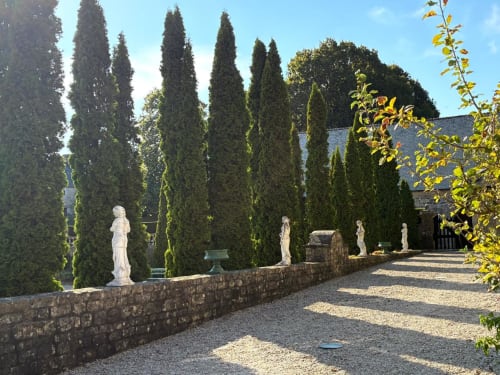 Allée formelle du Château de Servigny bordée de cyprès élancés, de statues blanches et de murs en pierre