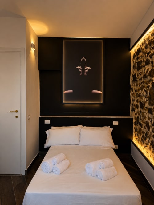 Camera moderna all'hotel Habemus di Rocca di Papa con testata nera, cuscini bianchi, asciugamani arrotolati e arte illuminata