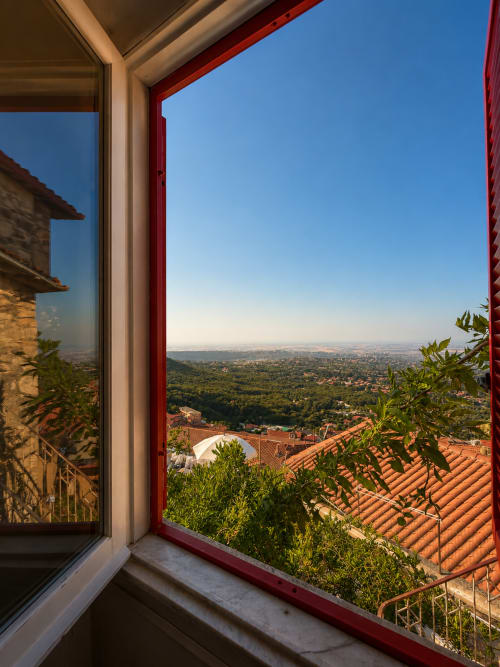 Finestra con telaio rosso che affaccia sui tetti di cotto e le vallate verdeggianti di Rocca di Papa, vista dalla camera dell'hotel Habemus