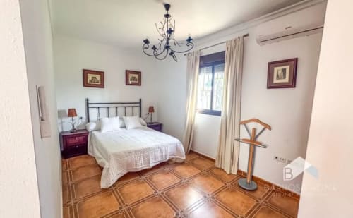 Elegante dormitorio de Barrosa Home con cama de hierro forjado, pisos de barro cocido y mobiliario en tonos crema