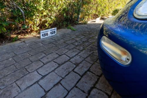 Automóvil azul estacionado en entrada de ladrillos en Barrosa Home con marcador de propiedad 136 125 visible