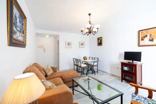 Sala de estar Barrosa con sofá beige, mesa de comedor, televisor y cuadros enmarcados en paredes blancas