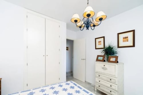 Dormitorio luminoso en Barrosa Home con ropa de cama de estrellas azules, muebles blancos, lámpara decorativa y cuadros enmarcados