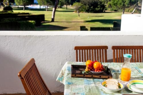 Terraza de comedor al aire libre en Barrosa Home con sillas de madera, fruta fresca, zumo y vistas a los jardines españoles