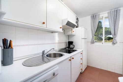 Cocina moderna y luminosa en Barrosa Home con armarios blancos, fregadero de acero inoxidable y piso de baldosas de terracota