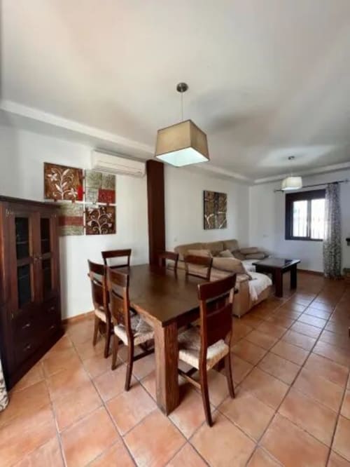 Zona abierta de comedor y sala de estar en Barrosa Home con mesa de madera, sillas y sofá beige