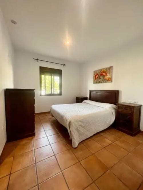 Amplio dormitorio en Barrosa Home con cama queen, muebles de madera oscura, baldosas de terracota y luz natural