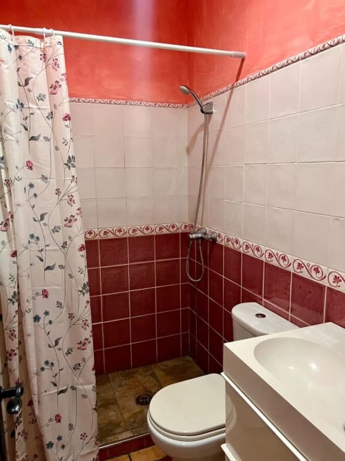 Baño de Barrosa Home con azulejos rojo y blanco, ducha con cortina floral, inodoro y lavamanos