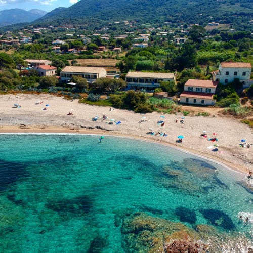 Hôtel Thalassa en bord de mer à Cargèse avec eaux méditerranéennes turquoise, plage de sable et village montagnard dans la verdure