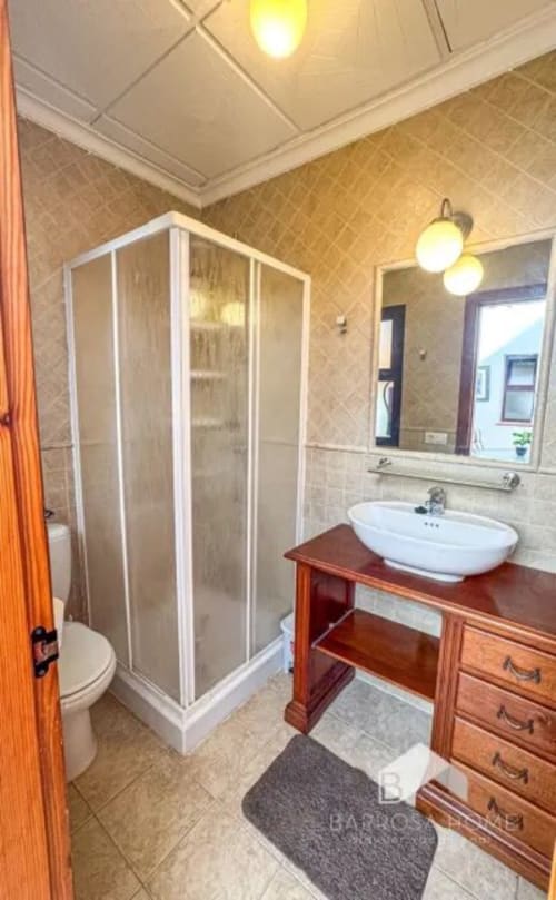 Baño moderno en Barrosa Home con ducha a ras de suelo, lavabo ovalado blanco sobre tocador de madera, espejo y toallero climatizado.