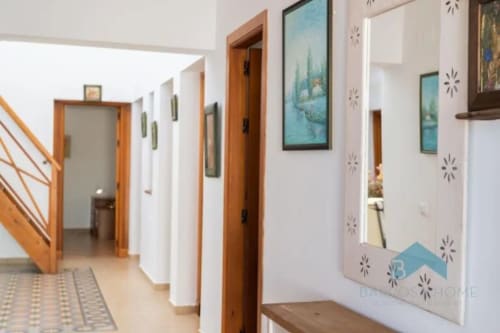 Luminoso pasillo en Barrosa Home con puertas de madera, paredes blancas, obras de arte enmarcadas y espejo decorativo