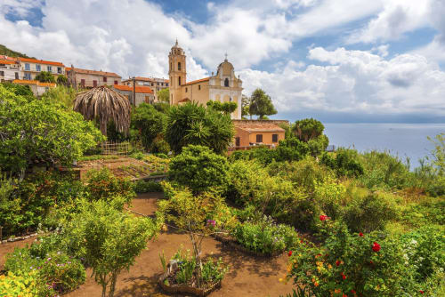 Jardin méditerranéen luxuriant avec bâtiments en terre cuite et église surplombant la mer à l'Hôtel Thalassa, Cargèse