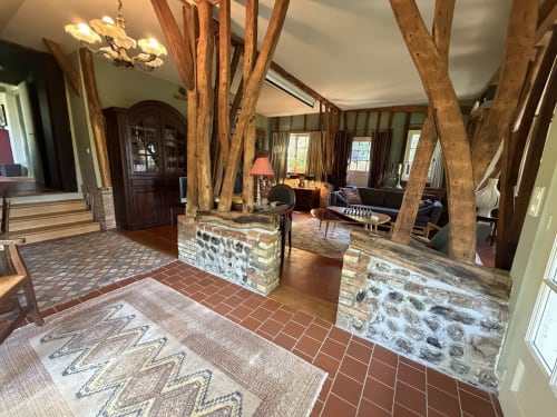 Entrée de villa rustique aux poutres bois apparentes, piliers en pierre, carrelage en terre cuite et vue sur le jardin à Varengeville-sur-Mer