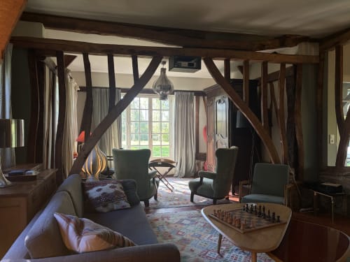 Élégant séjour de villa avec poutres apparentes, fauteuils verts, table d'échecs et vue sur le jardin