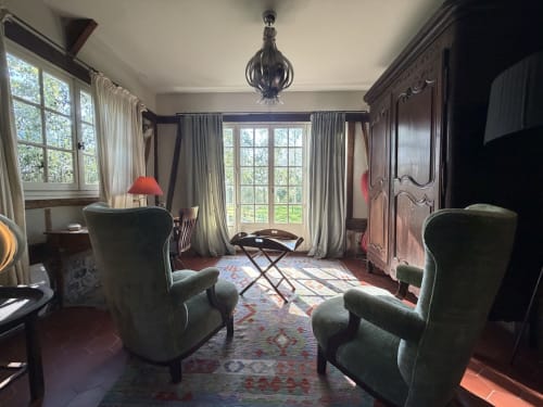 Élégante chambre de villa à Mon Week End A La Mer avec fauteuils verts, mobilier en bois foncé, grandes fenêtres vue jardin