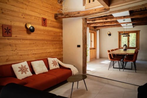 Chalet Névalia lounge with red sofa, wooden beams, and dining area in Ceillac