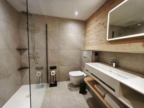 Modern bathroom in Chalet Névalia with glass shower, wall-mounted sink, toilet, and wooden accents