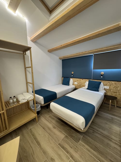 Chambre twin de l'Hotel Oreneta Gironella avec deux lits simples, poutres en bois, tête de lit bleu foncé et équipements modernes