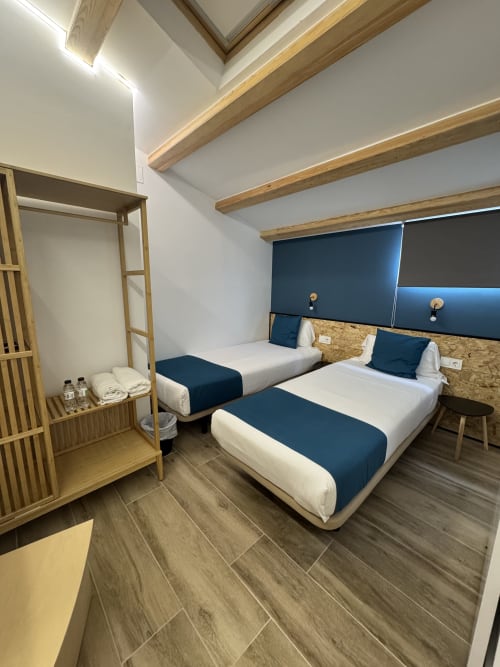 Chambre twin moderne à l'Hôtel Oreneta avec deux lits, poutres en bois, accents bleus et armoire en bois à Gironella.
